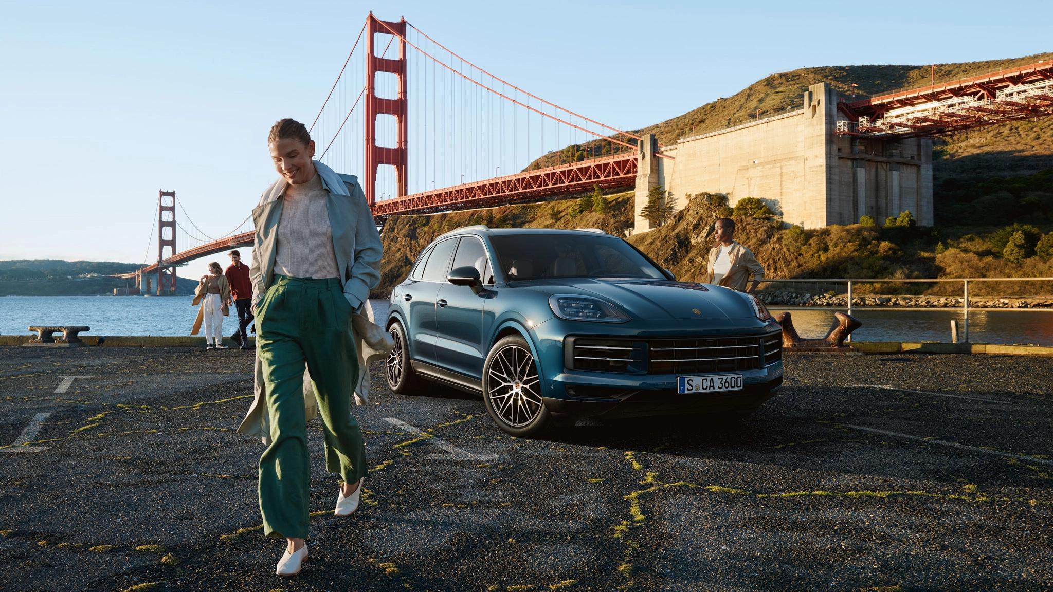 Porsche Cayenne S parkt mit der Golden Gate Bridge im Hintergrund und einer lächelnden Frau im Vordergrund